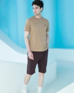 ست مردانه شامل تیشرت آستین کوتاه قهوه‌ای با چاپ برجسته کوهستان روی سینه و شلوارک تیره پشت دورس، تن‌خور مدل در محیط مدرن.