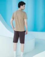 ست مردانه شامل تیشرت آستین کوتاه قهوه‌ای با چاپ برجسته کوهستان روی سینه و شلوارک تیره پشت دورس، تن‌خور مدل در محیط مدرن.